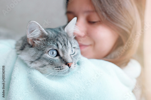 Beautiful woman at home holding and hug her lovely fluffy cat. Gray tabby cute kitten with blue eyes. Friend of human. Good sunny morning.