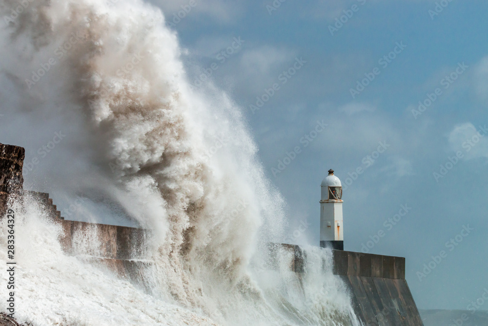 Huge ocean waves crashing into a sea wall and lighthouse (Porthcawl, South Wales, UK)