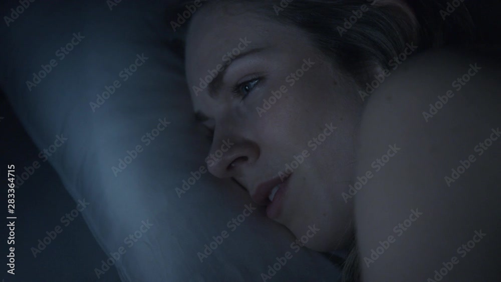 Close-up pan from mobile phone to a young woman face as she lies in bed at night using her mobile phone. Concept: Bad sleep health Close-up pan from mobile phone to a young woman face as she lies in bed at night using her mobile phone. Concept: Bad sleep health