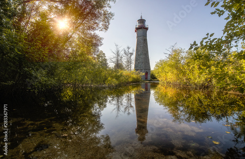 Photography Beautiful golden light shining on a stone lighthouse, reflecting in water surrounding by lush green trees