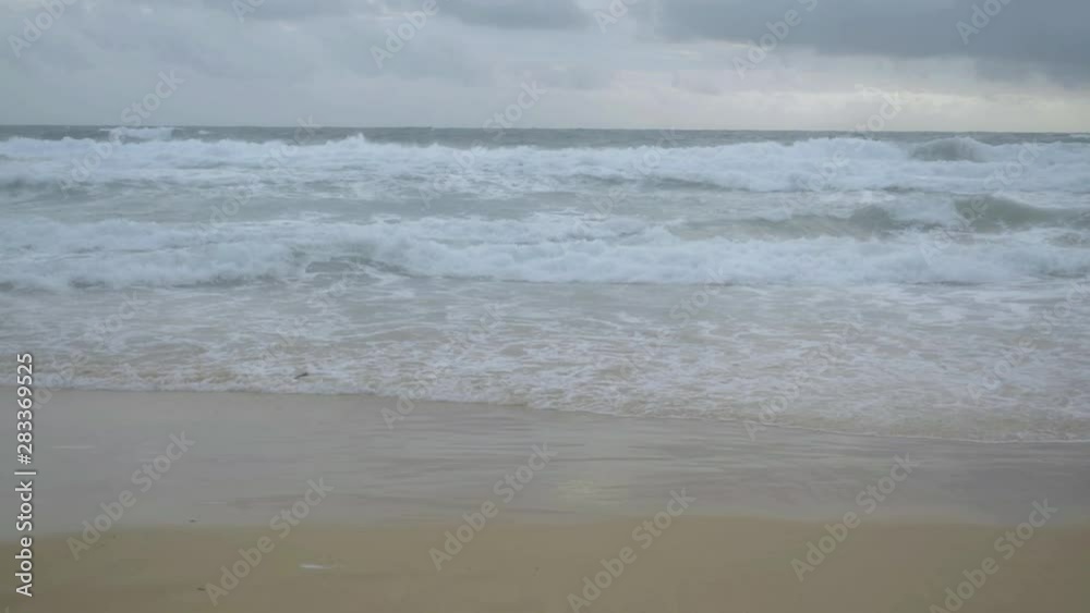 Scenery of tropical sandy beach with foam formed by waves breaking on a seashore and rain clouds in the sky at karon beach, Phuket, Thailand. Scenery of tropical sandy beach with foam formed by waves breaking on a seashore and rain clouds in the sky at karon beach, Phuket, Thailand.