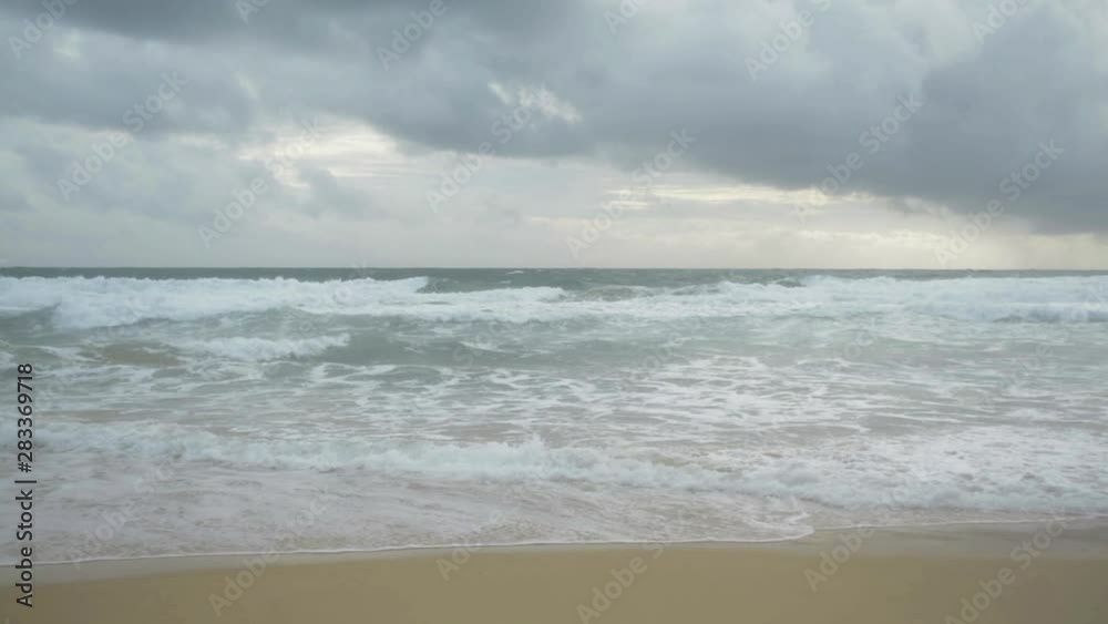 Scenery of tropical sandy beach with foam formed by waves breaking on a seashore and rain clouds in the sky at karon beach, Phuket, Thailand. Scenery of tropical sandy beach with foam formed by waves breaking on a seashore and rain clouds in the sky at karon beach, Phuket, Thailand.