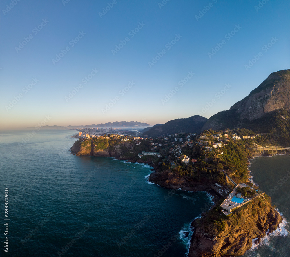 Panoramic view of the coastline of Joatinga in Rio de Janeiro with its beautiful natural richness and Costa Brava social club with pool in the foreground on a small island against a blue sky