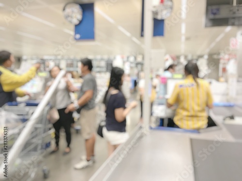 Blurred image of cashier with long line of people at check-out counter for sale, payment of wholesale store, Customers paying with credit card to store clerks, full cart of groceries. Cashier register