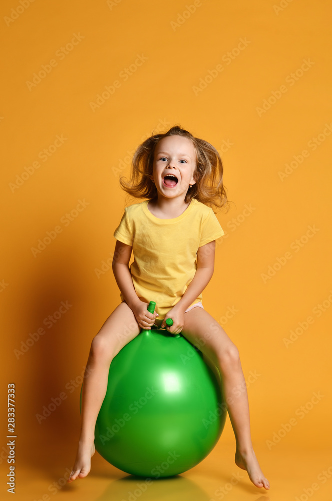 Little sporty girl child in shorts and t-shirt plays jumps on the fit ball.