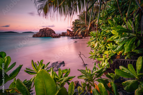Beautiful romantic sunset sundown red sky on Seychelles paradise island. Granite rocks, palm trees and white sand beach