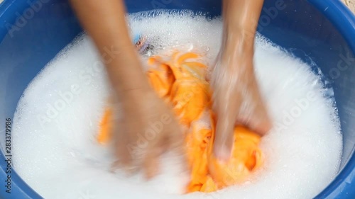 Man hands washing yellow color clothes in blue basin.