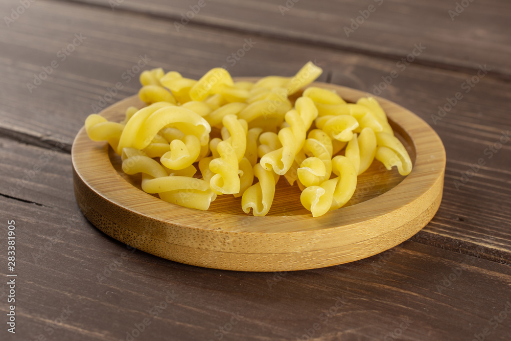 Lot of whole raw pasta gemelli on bamboo plate on brown wood