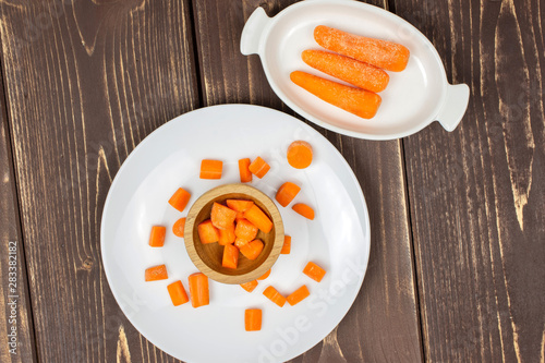 Fototapeta Naklejka Na Ścianę i Meble -  Group of three whole lot of pieces of stale  orange stale baby carrot baby on white porcelain plate flatlay isolated on brown wood