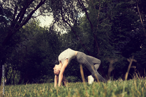 Young sporty attractive woman practicing yoga, doing Wild Thing, Flip-the-Dog exercise, Camatkarasana pose, working out, wearing sportswear, black pants and top, indoor full length