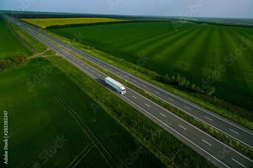 white trucks on the higthway sunset. cargo delivery driving on asphalt road along the green fields. seen from the air. Aerial view landscape. drone photography.