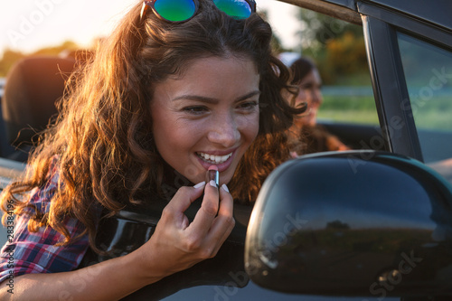 Beautiful young woman putting on lipstick in the front seat of a car