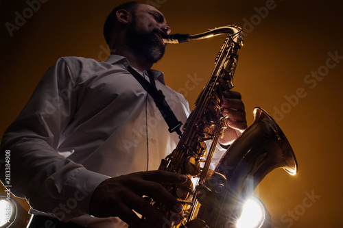 Portrait of professional musician saxophonist man in white shirt plays jazz music on saxophone, yellow background in a photo studio, bottom view