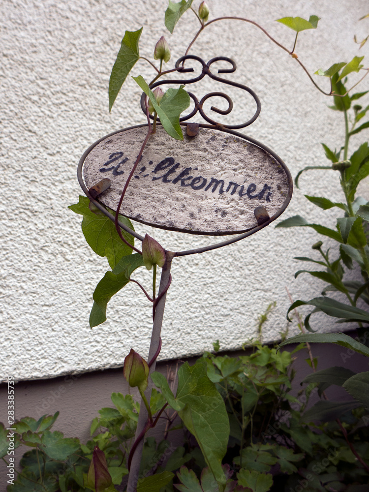 Ein Schild mit der Aufschrift Willkommen ist von Rankpflanzen