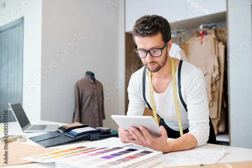 Young confident fashion designer with tablet scrolling through online ideas