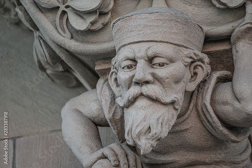 Foto Sculpture of an old small and bearded funny man, dwarf, as an atlant in downtown