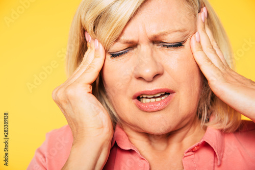 Portrait of beautiful blonde senior woman with severe headache while she holds hands on her head with closed eyes.