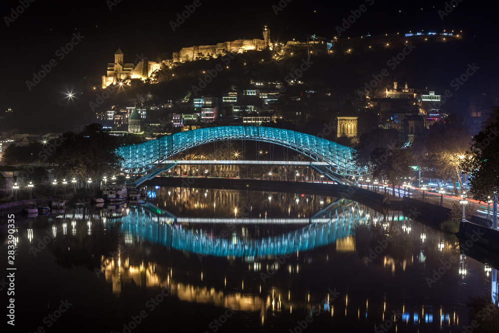 Pedestrian bridge of peace over the Mtkvari (Kura) River in Tbilisi at night. Narikala fortress.