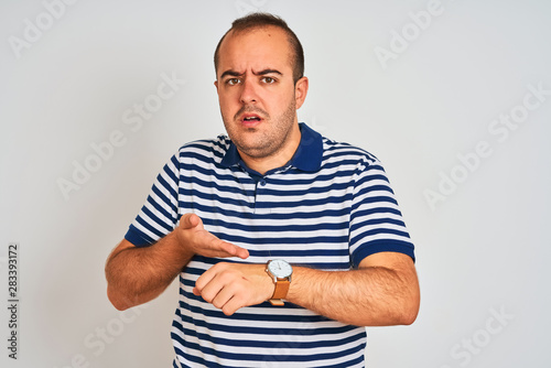 Young man wearing casual striped polo standing over isolated white background In hurry pointing to watch time, impatience, upset and angry for deadline delay