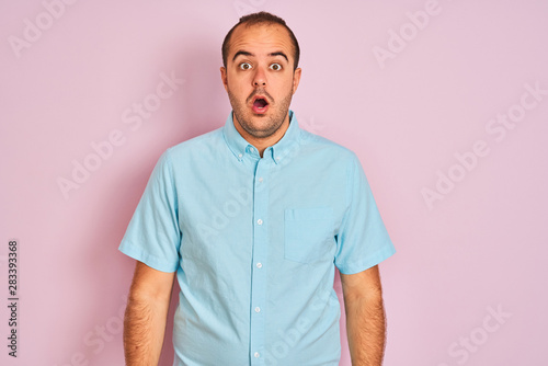 Young man wearing blue casual shirt standing over isolated pink background afraid and shocked with surprise expression, fear and excited face.