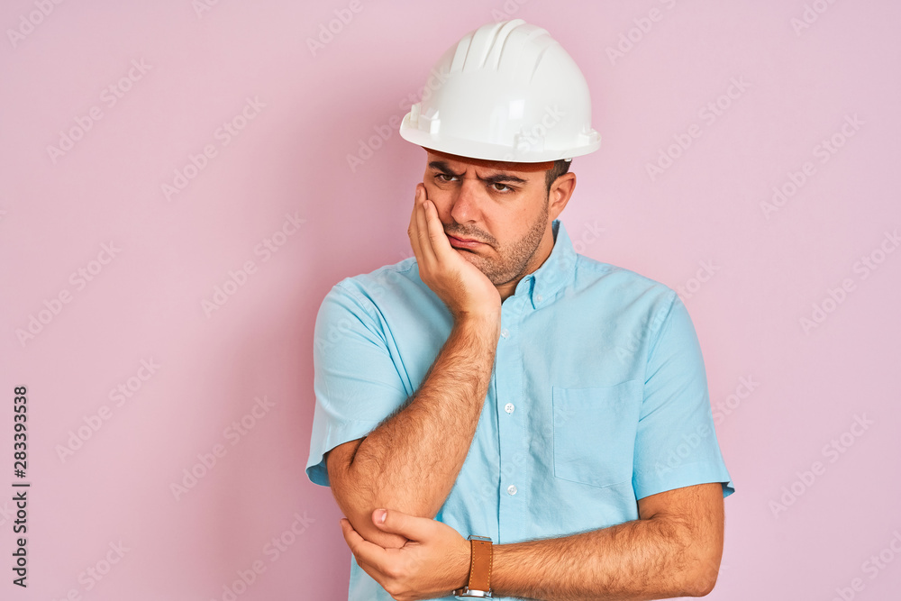 Young architect man wearing security helmet standing over isolated pink background thinking looking tired and bored with depression problems with crossed arms.