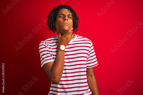 Young afro man with dreadlocks wearing striped t-shirt standing over isolated red background Touching painful neck, sore throat for flu, clod and infection
