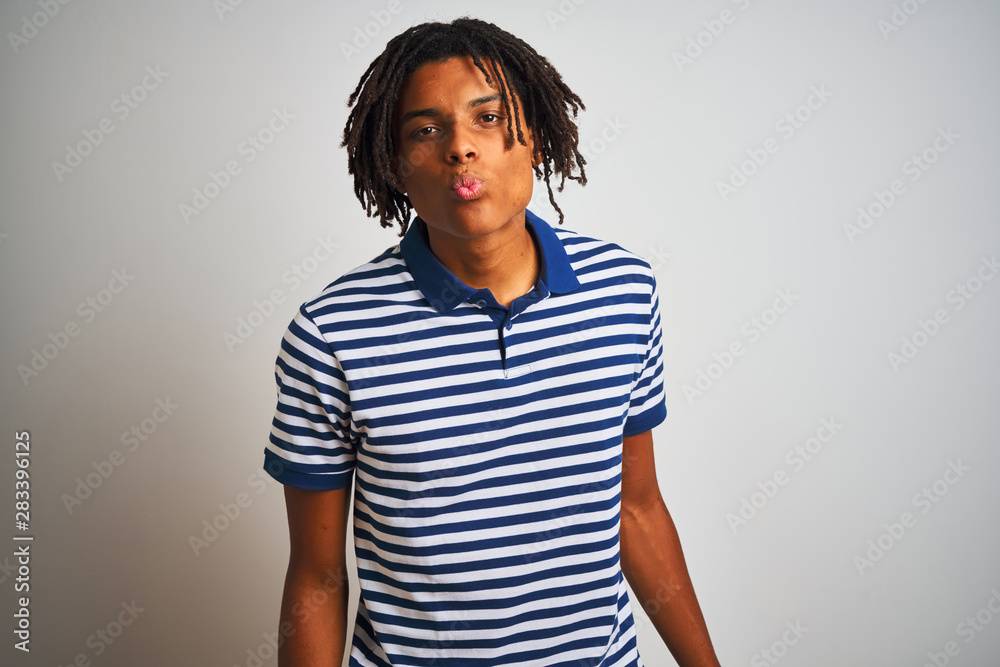Fototapeta premium Afro man with dreadlocks wearing striped blue polo standing over isolated white background looking at the camera blowing a kiss on air being lovely and sexy. Love expression.
