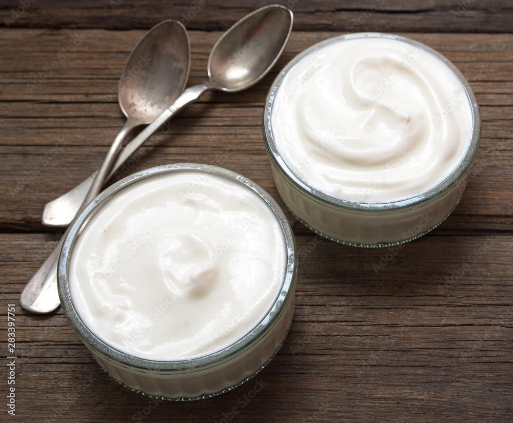 White yogurt in glass bowl on old wooden desk with old rustic spoon. White yogurt in glass bowl on old wooden desk with old rustic spoon.