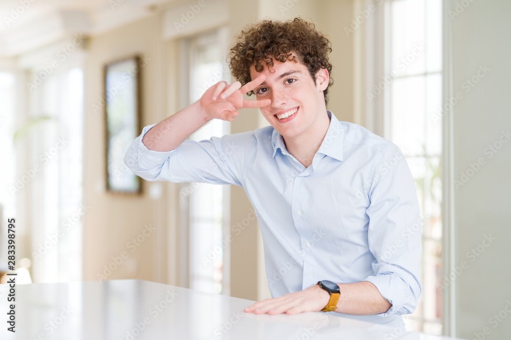 Young business man with curly read head Doing peace symbol with fingers over face, smiling cheerful showing victory