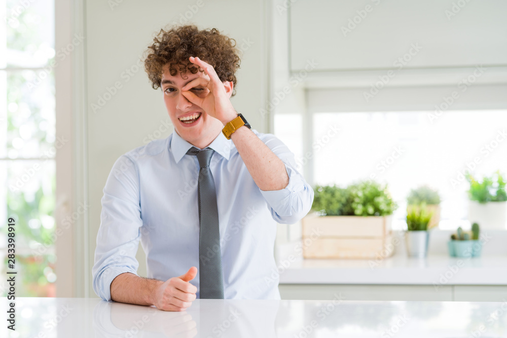 Young business man wearing a tie doing ok gesture with hand smiling, eye looking through fingers with happy face. Young business man wearing a tie doing ok gesture with hand smiling, eye looking through fingers with happy face.