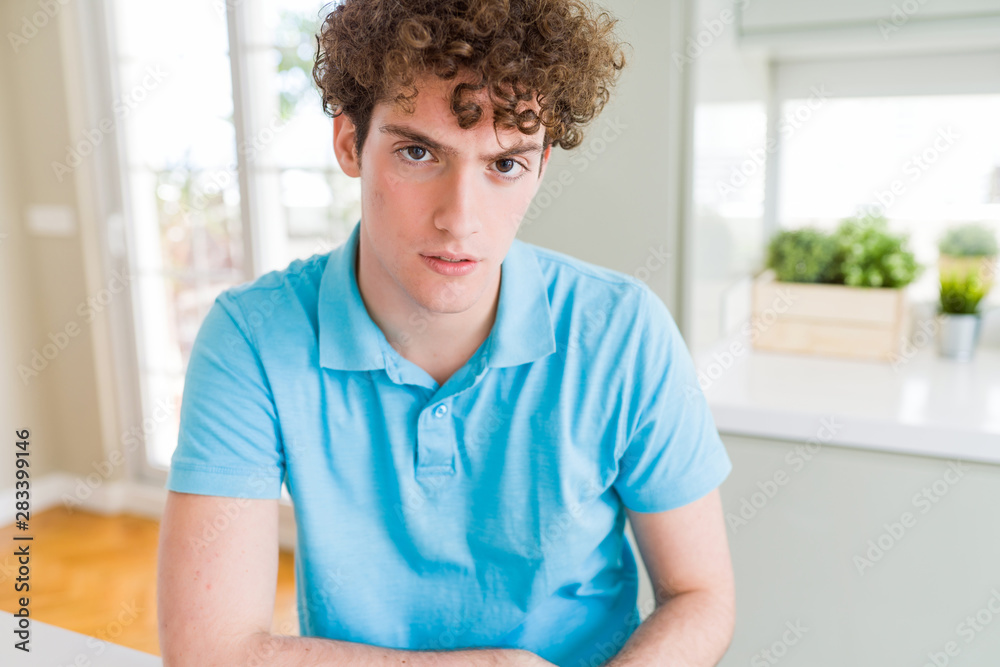 Fototapeta premium Young handsome man wearing casual blue t-shirt at home skeptic and nervous, disapproving expression on face with crossed arms. Negative person.