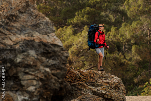 Woman standing on the rock with hiking backpack and walking sticks