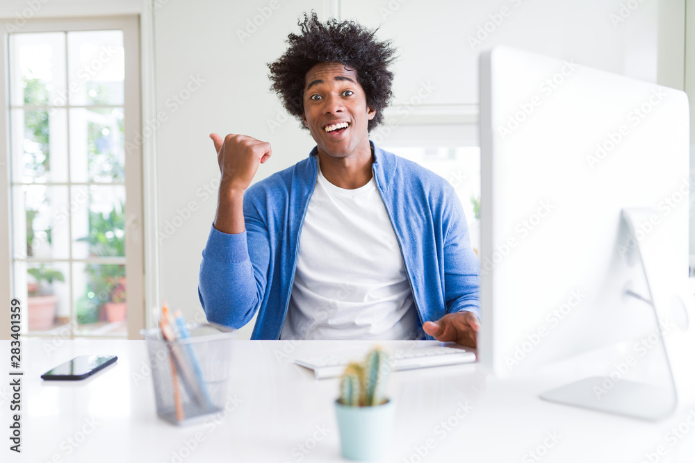 African American man working using computer pointing and showing with thumb up to the side with happy face smiling