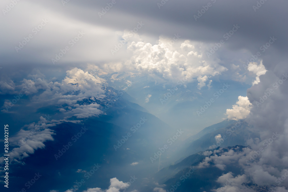 The bird's eye view on the sky with the huge fluffy dramatic clouds above the Alps.