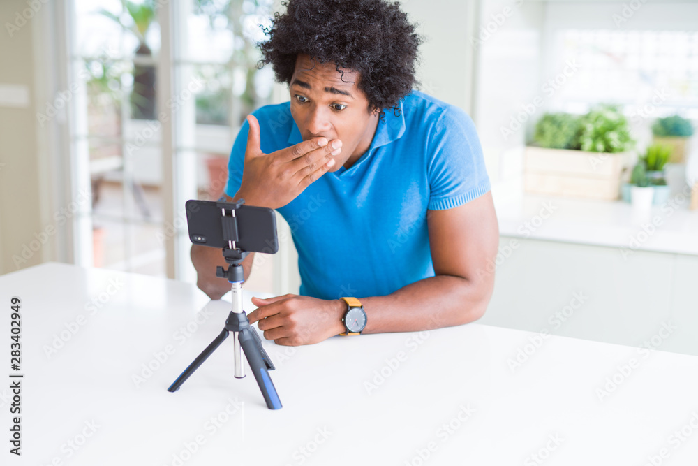 African American man doing online call with webcam using smartphone cover mouth with hand shocked with shame for mistake, expression of fear, scared in silence, secret concept African American man doing online call with webcam using smartphone cover mouth with hand shocked with shame for mistake, expression of fear, scared in silence, secret concept