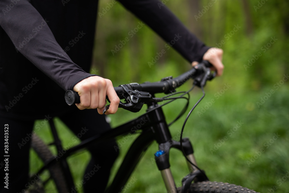 A man is riding a bicycle in a forest in the open air close-up. Park, active recreation, sports and a healthy lifestyle. Hands of a man on the wheel of a bicycle. Steering wheel bike close-up. A man is riding a bicycle in a forest in the open air close-up. Park, active recreation, sports and a healthy lifestyle. Hands of a man on the wheel of a bicycle. Steering wheel bike close-up.