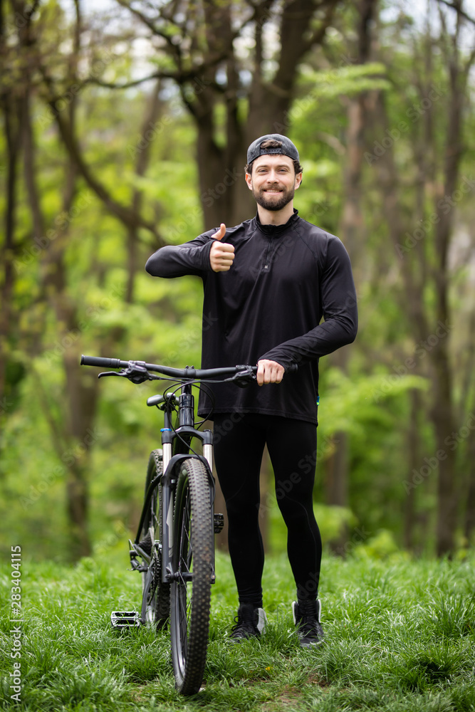 Happy man shows thumb up, riding on bicycle in forest, sport leisure. Cyclist walk in park, active healthy lifestyle