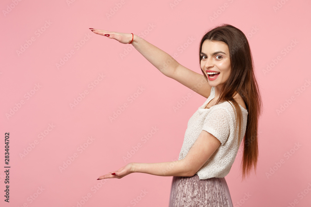 Funny young woman in casual light clothes posing isolated on pink wall background, studio portrait. People lifestyle concept. Mock up copy space. Gesturing demonstrating size with vertical workspace. Funny young woman in casual light clothes posing isolated on pink wall background, studio portrait. People lifestyle concept. Mock up copy space. Gesturing demonstrating size with vertical workspace.
