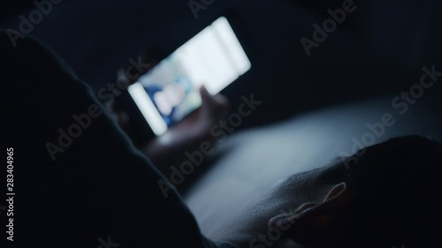 A man in bed at night using scrolling on his mobile phone with a bright screen.