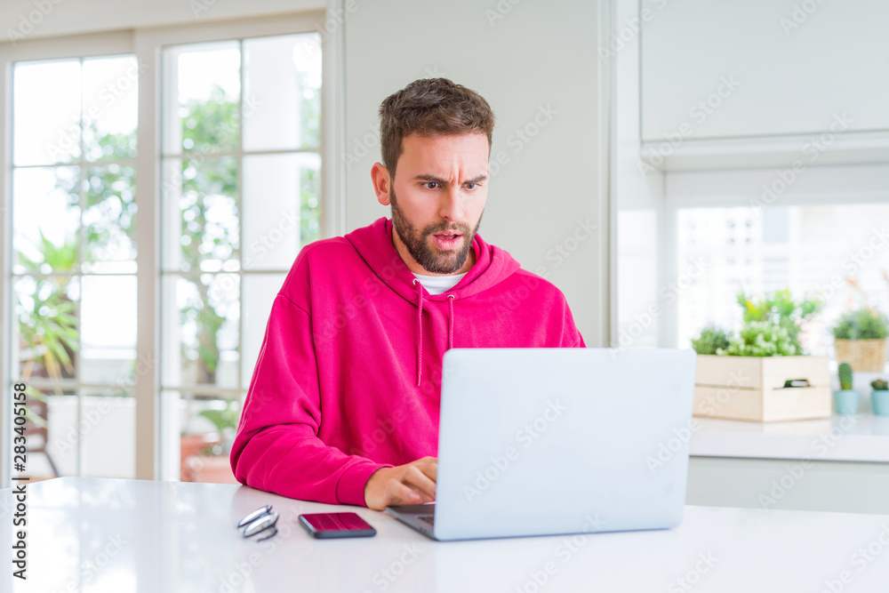 Handsome man working using computer laptop afraid and shocked with surprise expression, fear and excited face. Handsome man working using computer laptop afraid and shocked with surprise expression, fear and excited face.