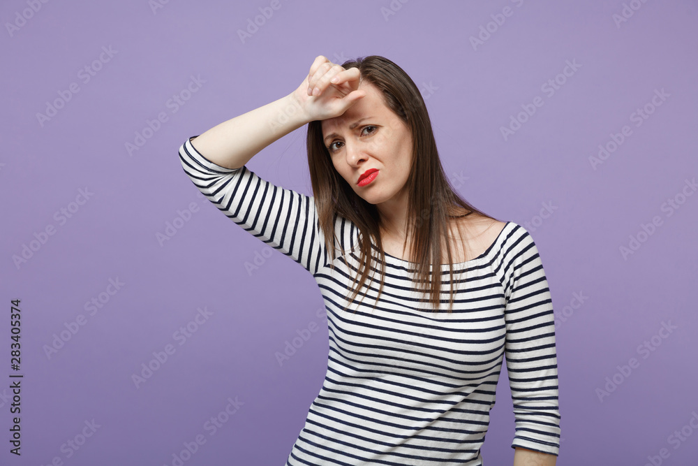 Tired exhausted young brunette woman girl in casual striped clothes posing isolated on violet purple background studio portrait. People lifestyle concept. Mock up copy space. Putting hand on forehead.