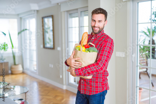 Handsome man holding paper bag full of fresh groceries at home photo