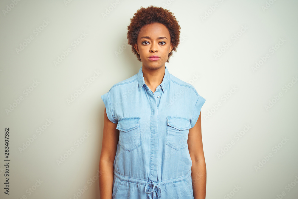 Young beautiful african american woman with afro hair over isolated background with serious expression on face. Simple and natural looking at the camera.