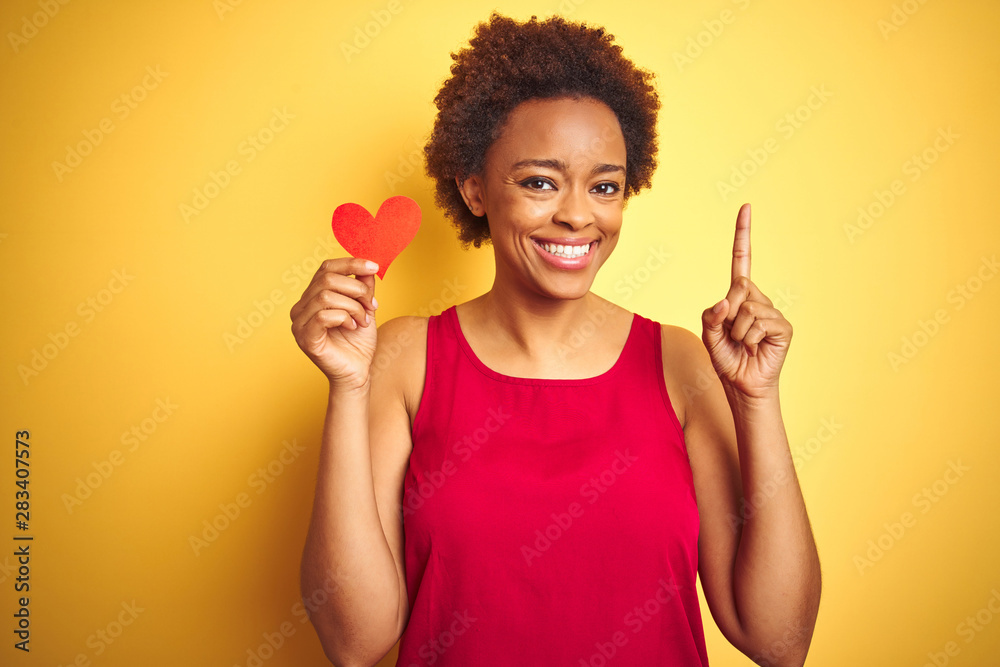 African american woman holding romantic paper hearts over yellow isolated background surprised with an idea or question pointing finger with happy face, number one