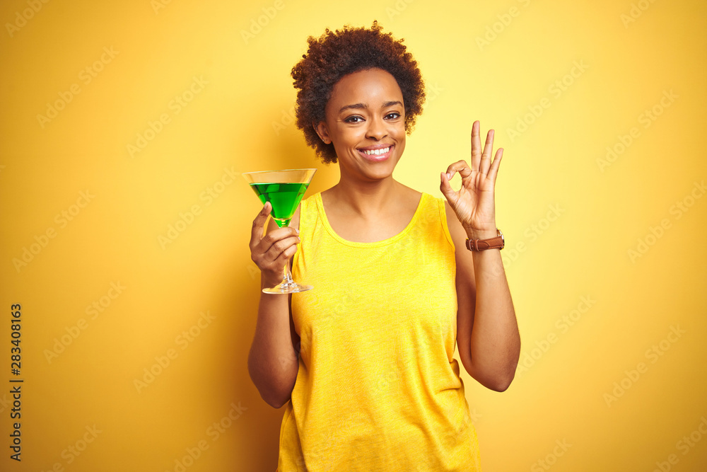 Young african american woman with afro hair drinking a cocktail over yellow isolated background doing ok sign with fingers, excellent symbol Young african american woman with afro hair drinking a cocktail over yellow isolated background doing ok sign with fingers, excellent symbol