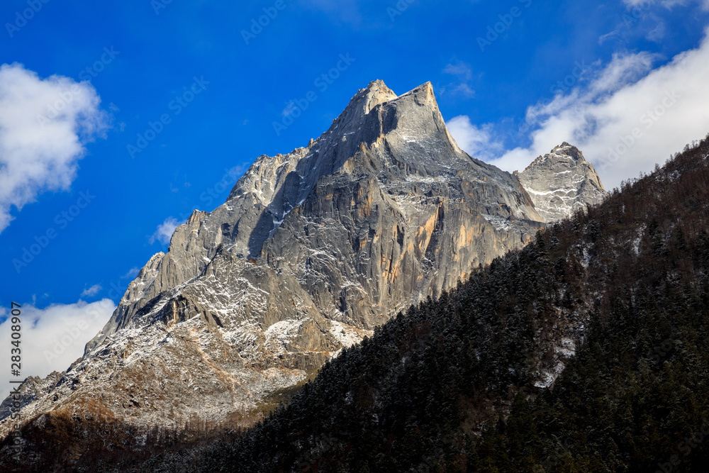 Siguniangshan - Four Girls Mountain National Park in Sichuan Province, China. ShuangQiao Valley Scenic Area, Snow Capped Jagged Mountains with clouds forming at the summit. Blue Sky, Snow Mountains