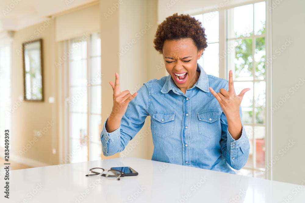 Young beautiful african american woman shouting with crazy expression doing rock symbol with hands up. Music star. Heavy concept.