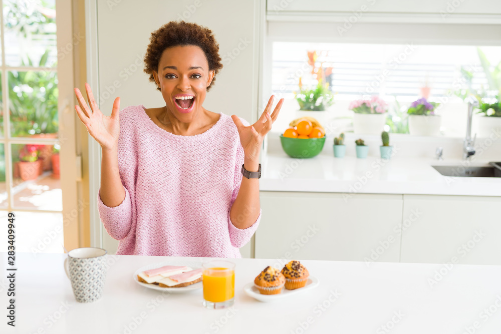 Young african american woman eating breaksfast in the morning at home celebrating crazy and amazed for success with arms raised and open eyes screaming excited. Winner concept