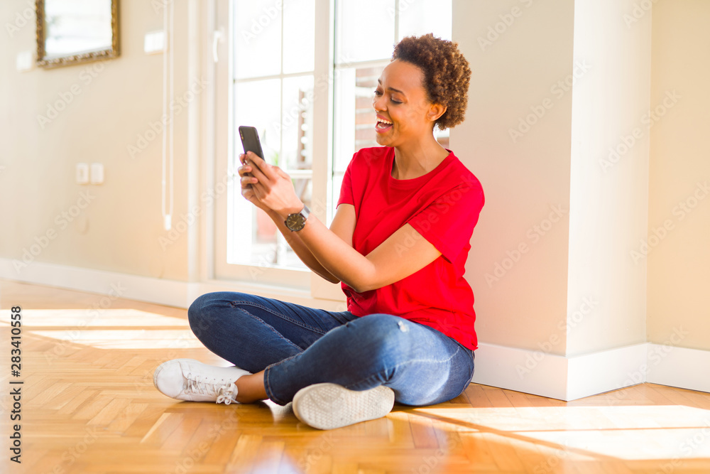 Beautiful young african american woman sitting on the floor using smartphone smiling
