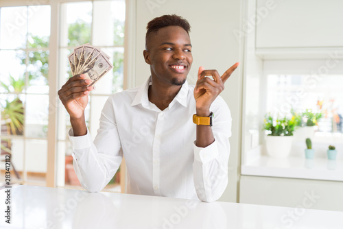 African american man holding fifty dollars bank notes very happy pointing with hand and finger to the side